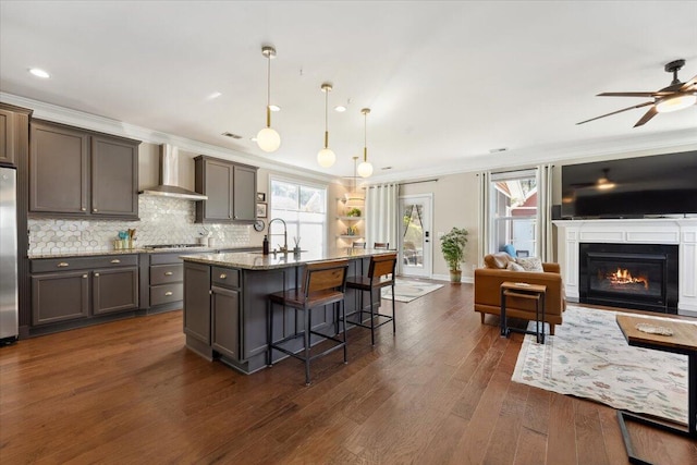 kitchen with wall chimney range hood, dark wood-type flooring, a kitchen breakfast bar, open floor plan, and backsplash