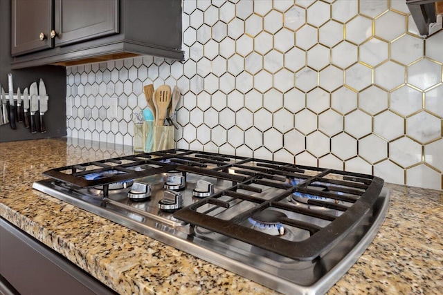 kitchen with light stone counters, backsplash, and stainless steel gas stovetop