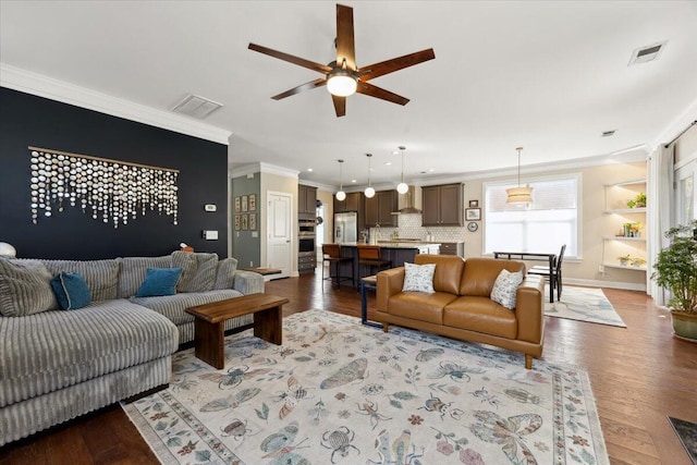 living area with baseboards, wood finished floors, visible vents, and ornamental molding