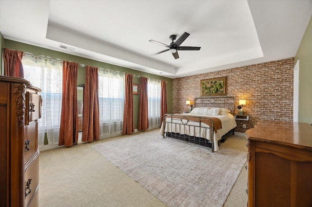 bedroom featuring visible vents, brick wall, ceiling fan, light colored carpet, and a raised ceiling