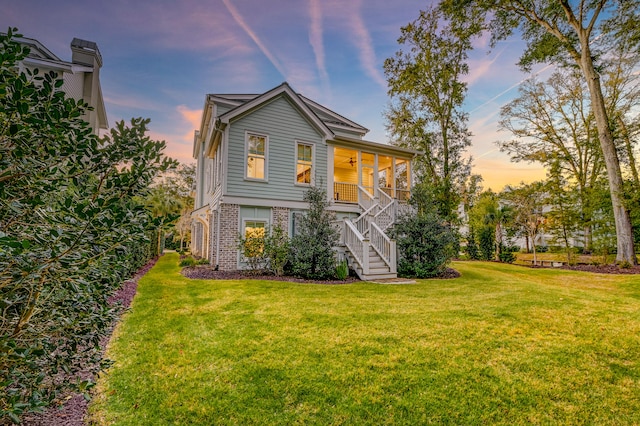 back house at dusk featuring a lawn, ceiling fan, and a porch