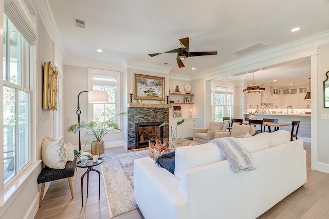 living room featuring crown molding, ceiling fan, a fireplace, and light wood-type flooring