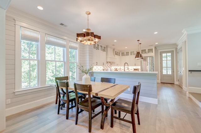 dining room with an inviting chandelier, sink, ornamental molding, and light hardwood / wood-style floors