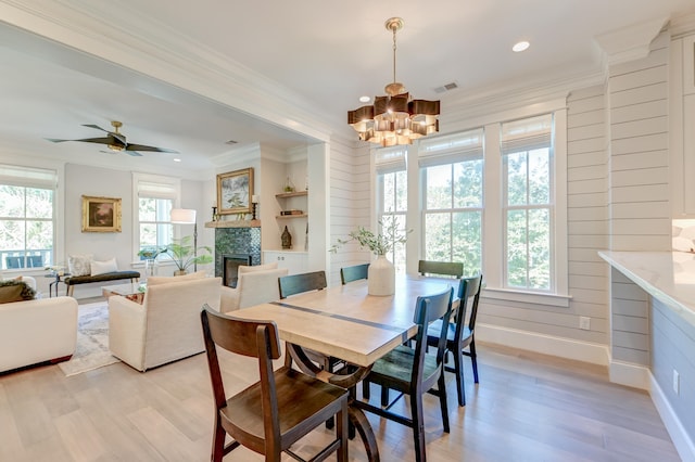 dining room featuring ornamental molding, a fireplace, ceiling fan with notable chandelier, and light wood-type flooring