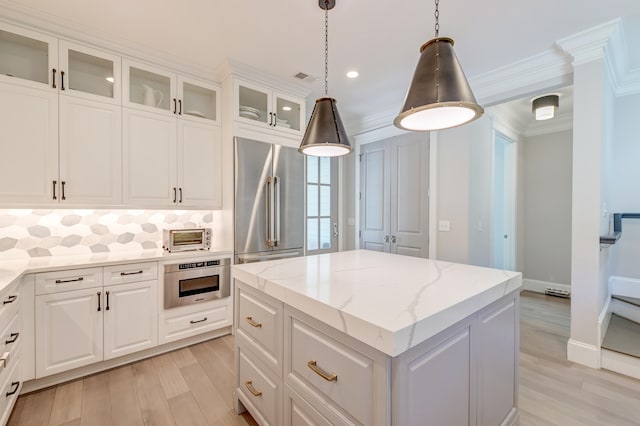 kitchen with crown molding, high quality fridge, a kitchen island, light stone countertops, and white cabinets