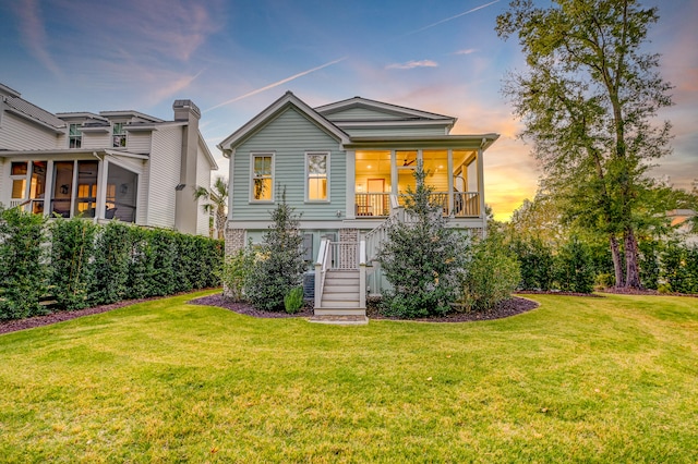 back house at dusk featuring a sunroom and a lawn