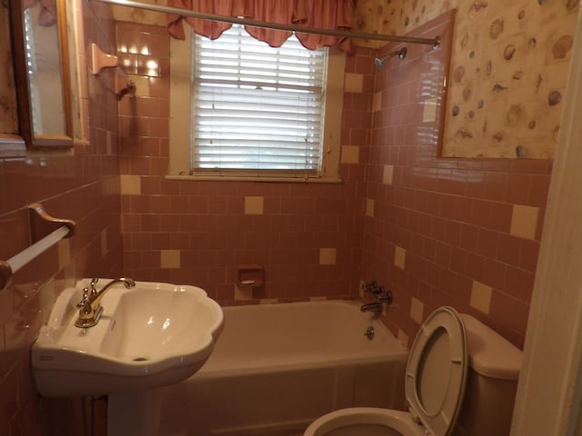 full bath with  shower combination, a sink, toilet, and tile walls