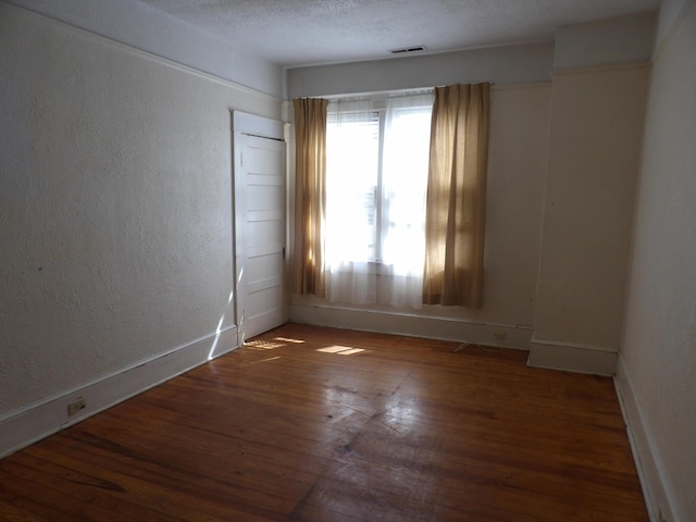 unfurnished room featuring visible vents, a textured wall, hardwood / wood-style floors, a textured ceiling, and baseboards