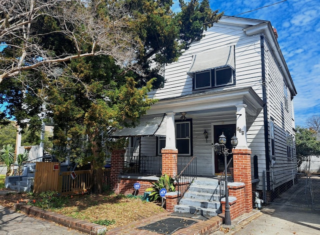 view of front of home featuring covered porch, brick siding, and fence