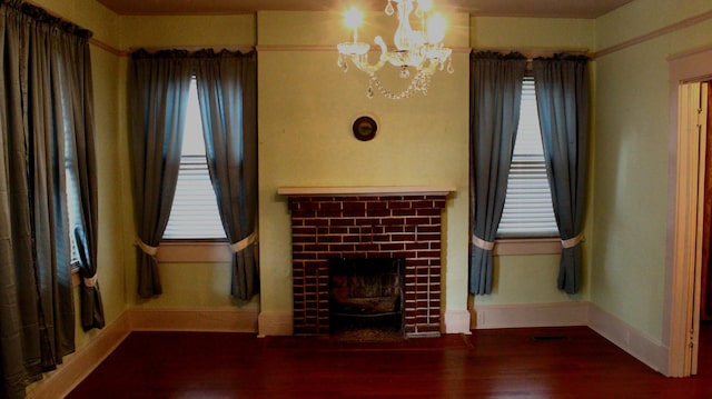 unfurnished living room featuring a healthy amount of sunlight, a notable chandelier, a fireplace, and wood finished floors