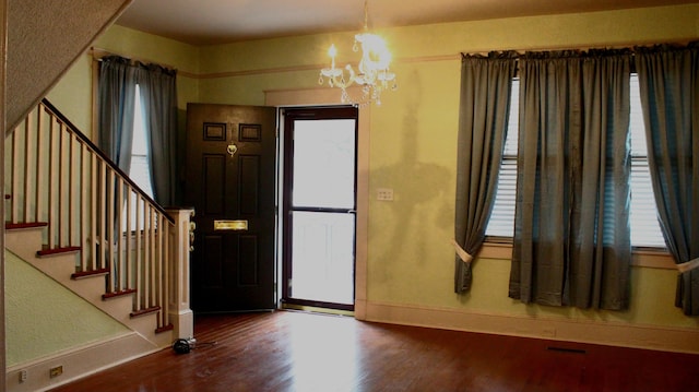 foyer entrance with stairs, a notable chandelier, baseboards, and wood finished floors