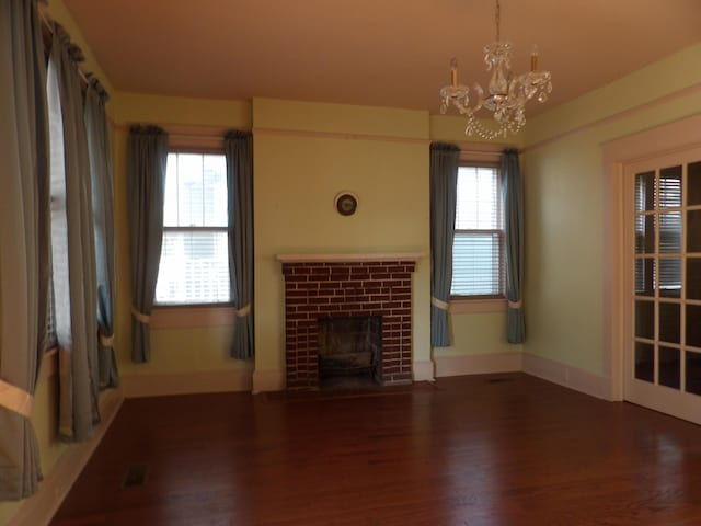 unfurnished living room with an inviting chandelier, a fireplace with flush hearth, a wealth of natural light, and wood finished floors