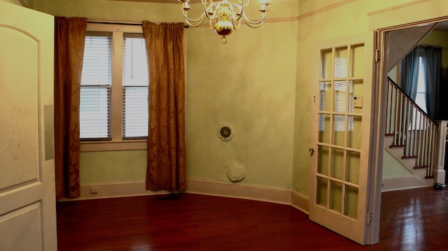 unfurnished room featuring a healthy amount of sunlight, baseboards, a chandelier, and wood finished floors