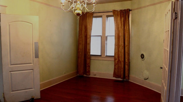 empty room featuring a chandelier, baseboards, and wood finished floors