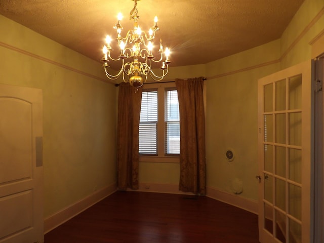 empty room with a notable chandelier, a textured ceiling, baseboards, and wood finished floors