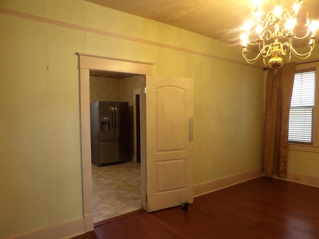 empty room with an inviting chandelier, baseboards, and wood finished floors