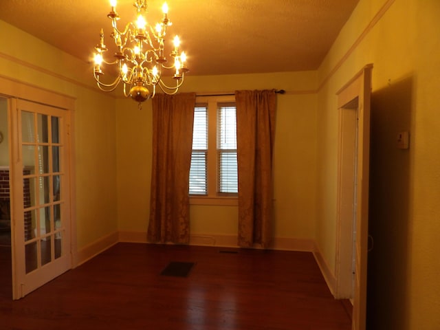 empty room featuring an inviting chandelier, visible vents, baseboards, and wood finished floors