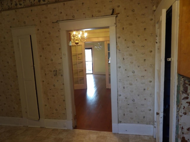 hallway featuring wallpapered walls, baseboards, wood finished floors, and an inviting chandelier