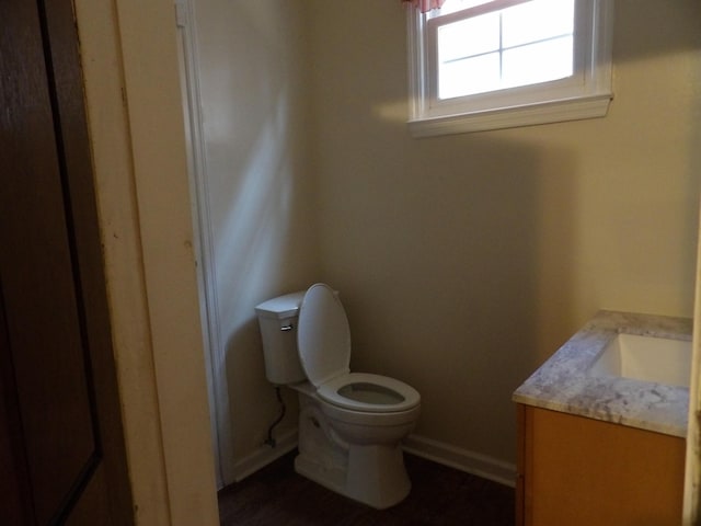 half bathroom with baseboards, vanity, and toilet