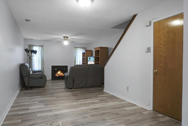 living room with ceiling fan, light hardwood / wood-style flooring, and a textured ceiling