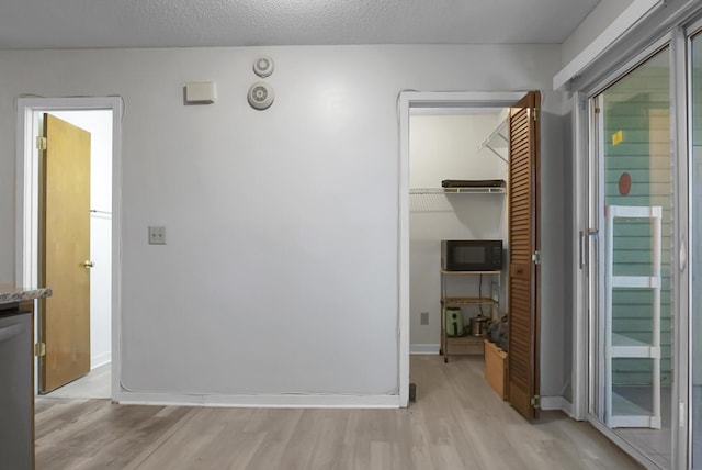 hallway with light hardwood / wood-style floors and a textured ceiling