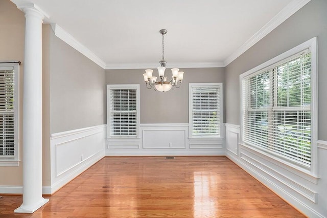 unfurnished dining area with crown molding, decorative columns, a healthy amount of sunlight, and light wood-type flooring