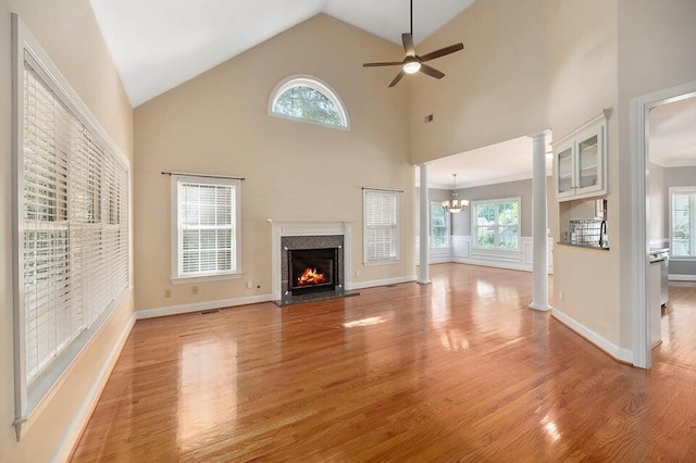 unfurnished living room featuring light hardwood / wood-style flooring, high vaulted ceiling, a high end fireplace, ceiling fan with notable chandelier, and ornate columns