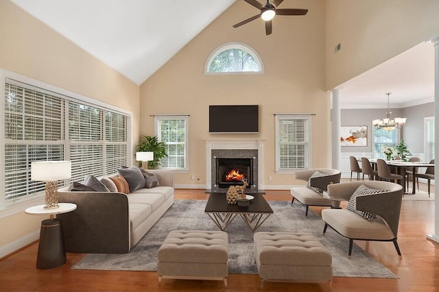 living room featuring high vaulted ceiling, ceiling fan with notable chandelier, a fireplace, and light hardwood / wood-style floors