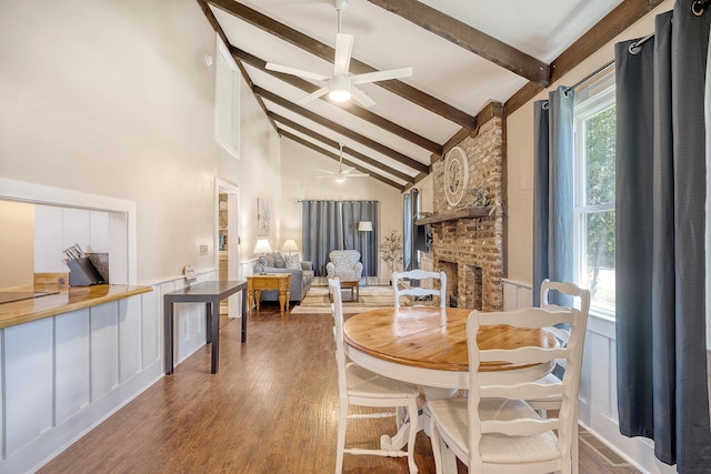 dining area featuring high vaulted ceiling, a fireplace, beam ceiling, ceiling fan, and hardwood / wood-style floors