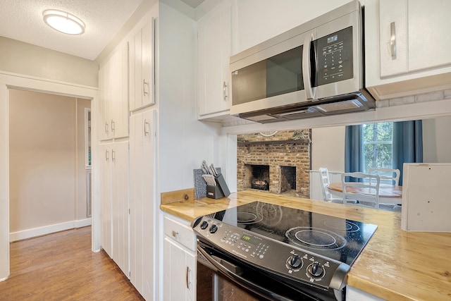 kitchen featuring appliances with stainless steel finishes, light hardwood / wood-style floors, a brick fireplace, white cabinets, and a textured ceiling