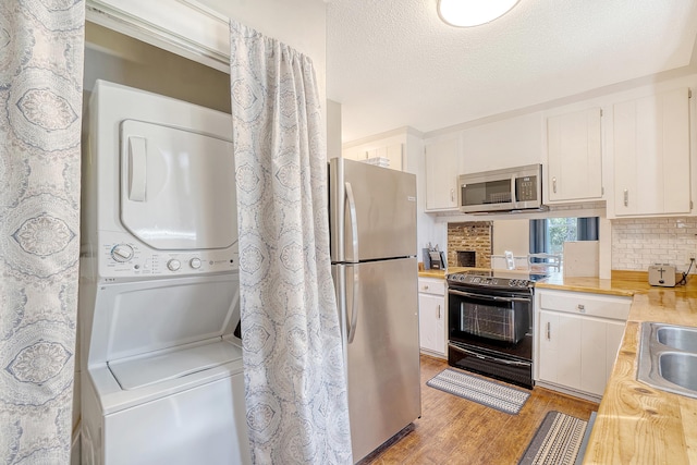 kitchen with stacked washer and clothes dryer, light hardwood / wood-style floors, white cabinetry, and stainless steel appliances