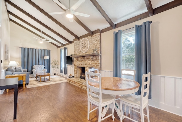 dining area featuring a brick fireplace, vaulted ceiling with beams, hardwood / wood-style flooring, and ceiling fan