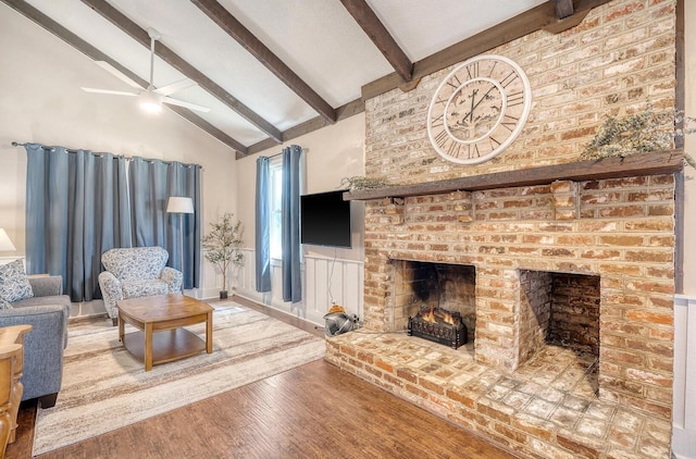 living room featuring vaulted ceiling with beams, ceiling fan, wood-type flooring, and a brick fireplace