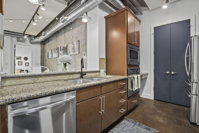 kitchen with concrete flooring, stone counters, a sink, appliances with stainless steel finishes, and rail lighting