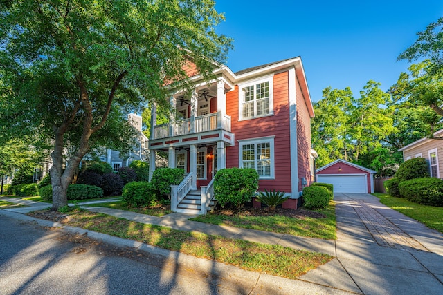 view of front of home with a detached garage, an outbuilding, ceiling fan, and a balcony