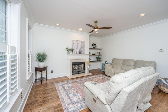 living area with crown molding, a tiled fireplace, a ceiling fan, recessed lighting, and wood finished floors
