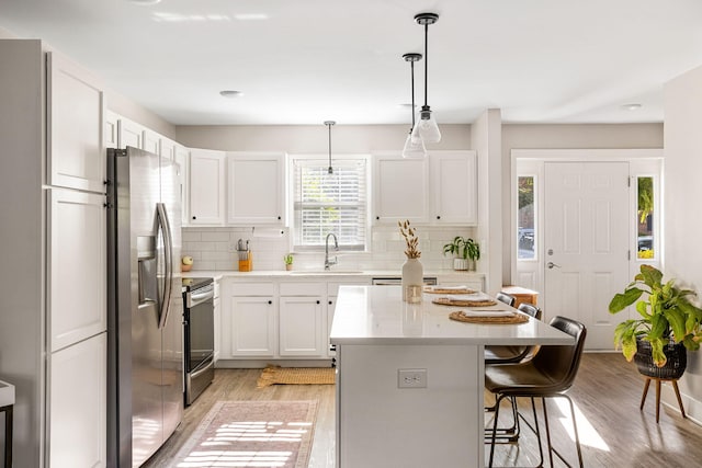 kitchen featuring pendant lighting, sink, light hardwood / wood-style flooring, appliances with stainless steel finishes, and white cabinetry