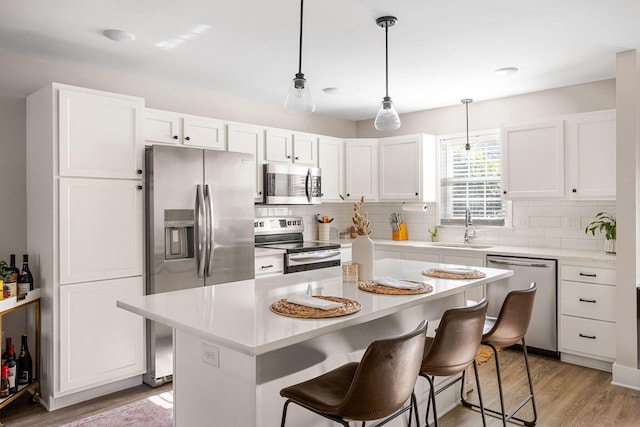 kitchen with sink, stainless steel appliances, a kitchen island, light hardwood / wood-style floors, and white cabinets