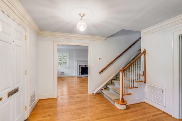 entrance foyer featuring a fireplace, light wood-type flooring, and ornamental molding