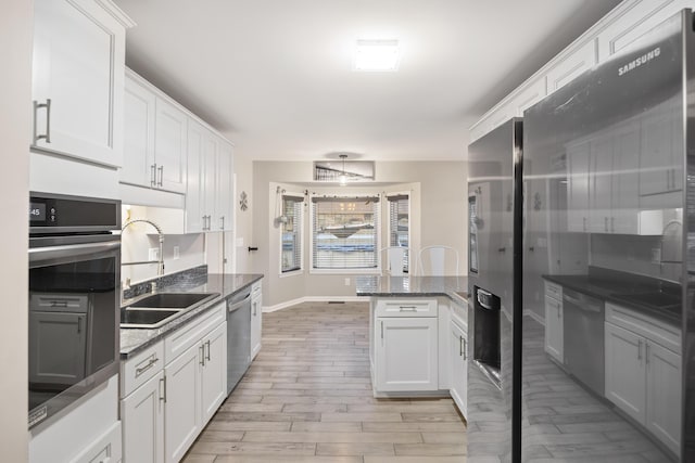 kitchen with sink, light hardwood / wood-style flooring, white cabinetry, dark stone countertops, and stainless steel appliances