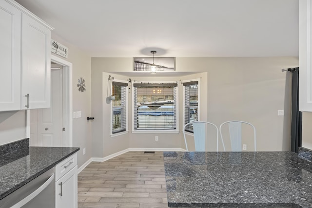 kitchen with dark stone countertops, dishwasher, light wood-type flooring, and white cabinets