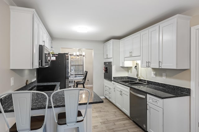 kitchen with sink, dark stone countertops, stainless steel appliances, white cabinets, and a chandelier