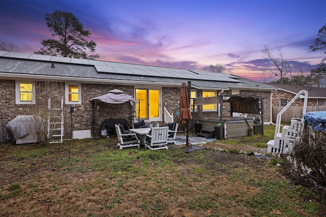 back house at dusk featuring a hot tub, a gazebo, and solar panels