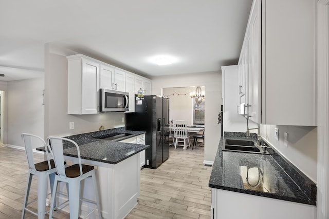 kitchen with a kitchen bar, dark stone countertops, stainless steel appliances, light hardwood / wood-style floors, and white cabinets