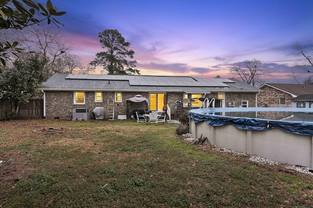 back house at dusk with a yard, solar panels, central AC, and a covered pool