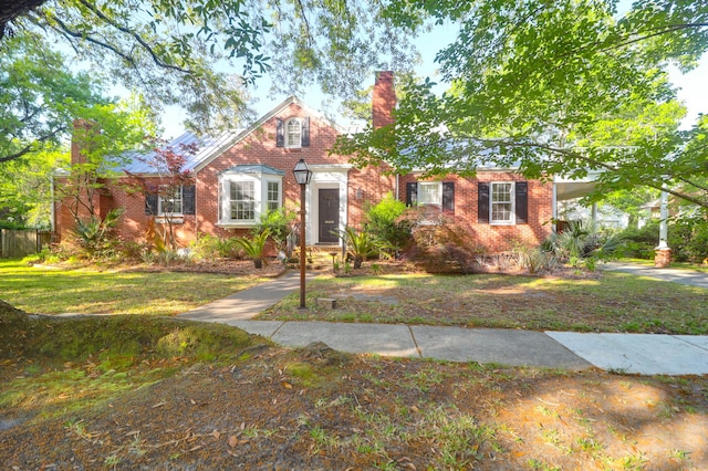 view of front of property with a chimney, a front lawn, brick siding, and fence
