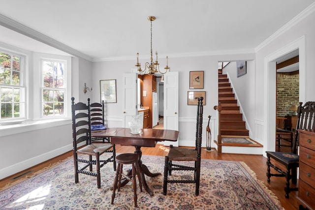 dining space with an inviting chandelier, wood finished floors, crown molding, baseboards, and stairs
