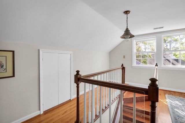 hallway with light wood finished floors, baseboards, visible vents, and an upstairs landing