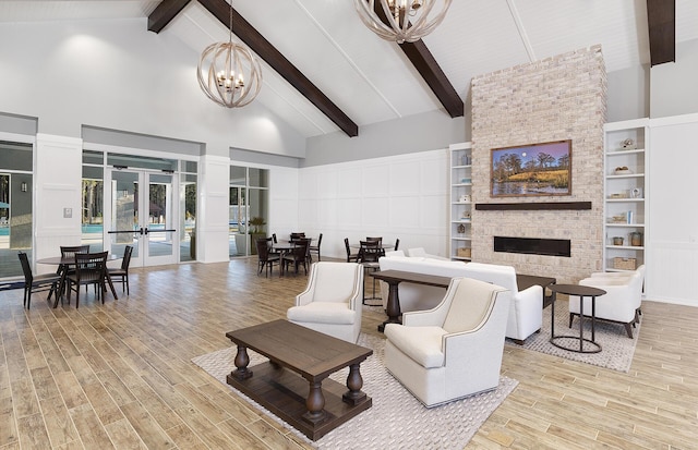 living room featuring high vaulted ceiling, a fireplace, wood finished floors, french doors, and a notable chandelier