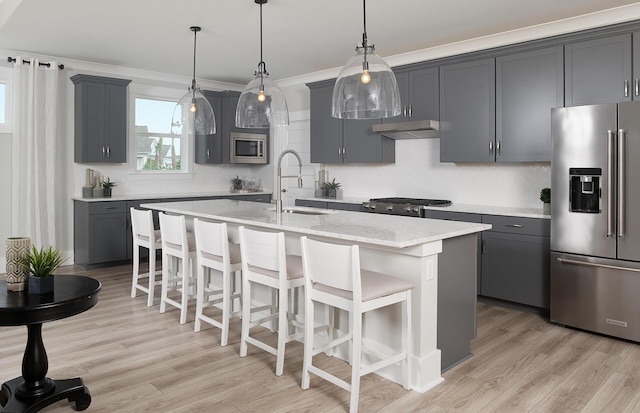 kitchen featuring a sink, a kitchen breakfast bar, appliances with stainless steel finishes, under cabinet range hood, and a kitchen island with sink